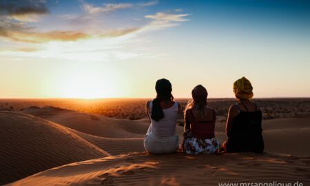 Drei Frauen blicken in den Sonnenuntergang in der Wüste